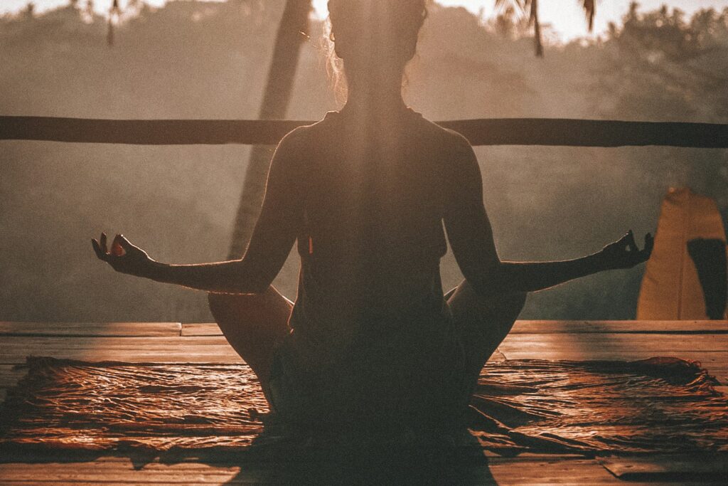 Donna seduta a gambe incrociate che medita su un tappetino da yoga in una stanza luminosa con pavimento in parquet